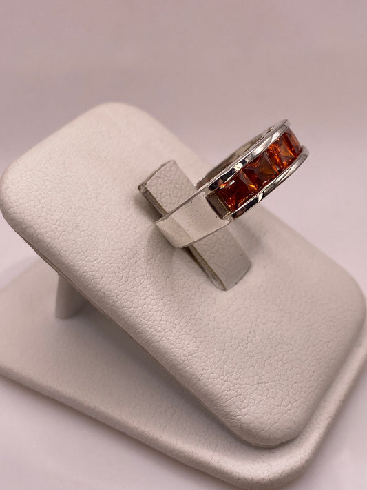 Vista lateral del anillo banda mostrando el perfil recto y el brillo de las circonias naranja en plata pulida