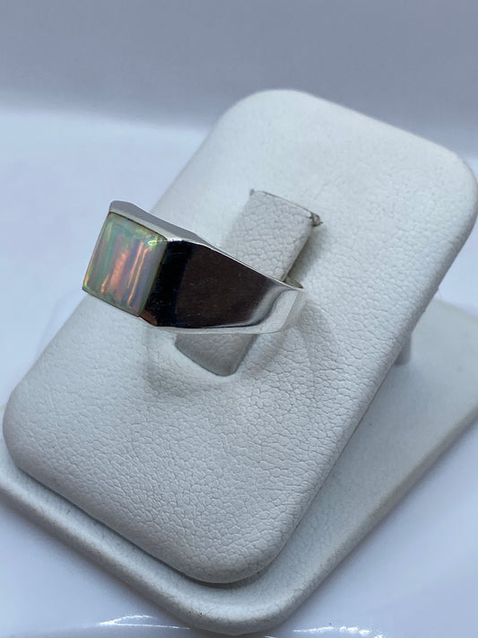 Anillo arquitectónico de plata en dedo con ópalo mostrando juego de colores naranja y verde