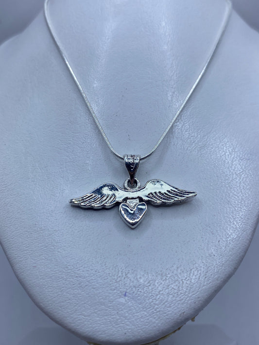 Detalle frontal del dije de alas y corazón mostrando el acabado pulido