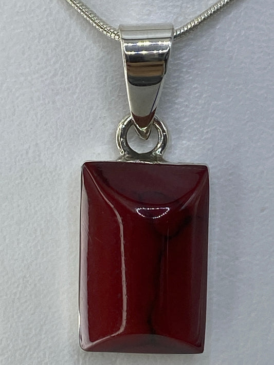 Detalle frontal del dije mostrando la incrustación de piedra roja pulida