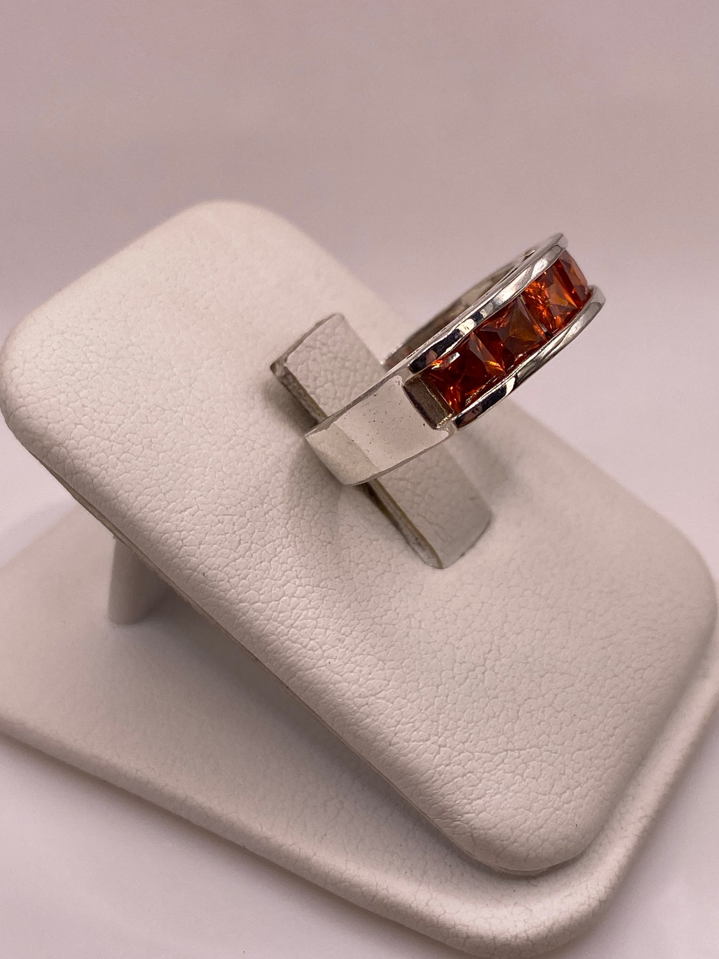 Vista lateral del anillo banda mostrando el perfil recto y el brillo de las circonias naranja en plata pulida
