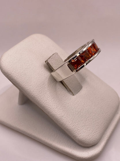 Vista lateral del anillo banda mostrando el perfil recto y el brillo de las circonias naranja en plata pulida
