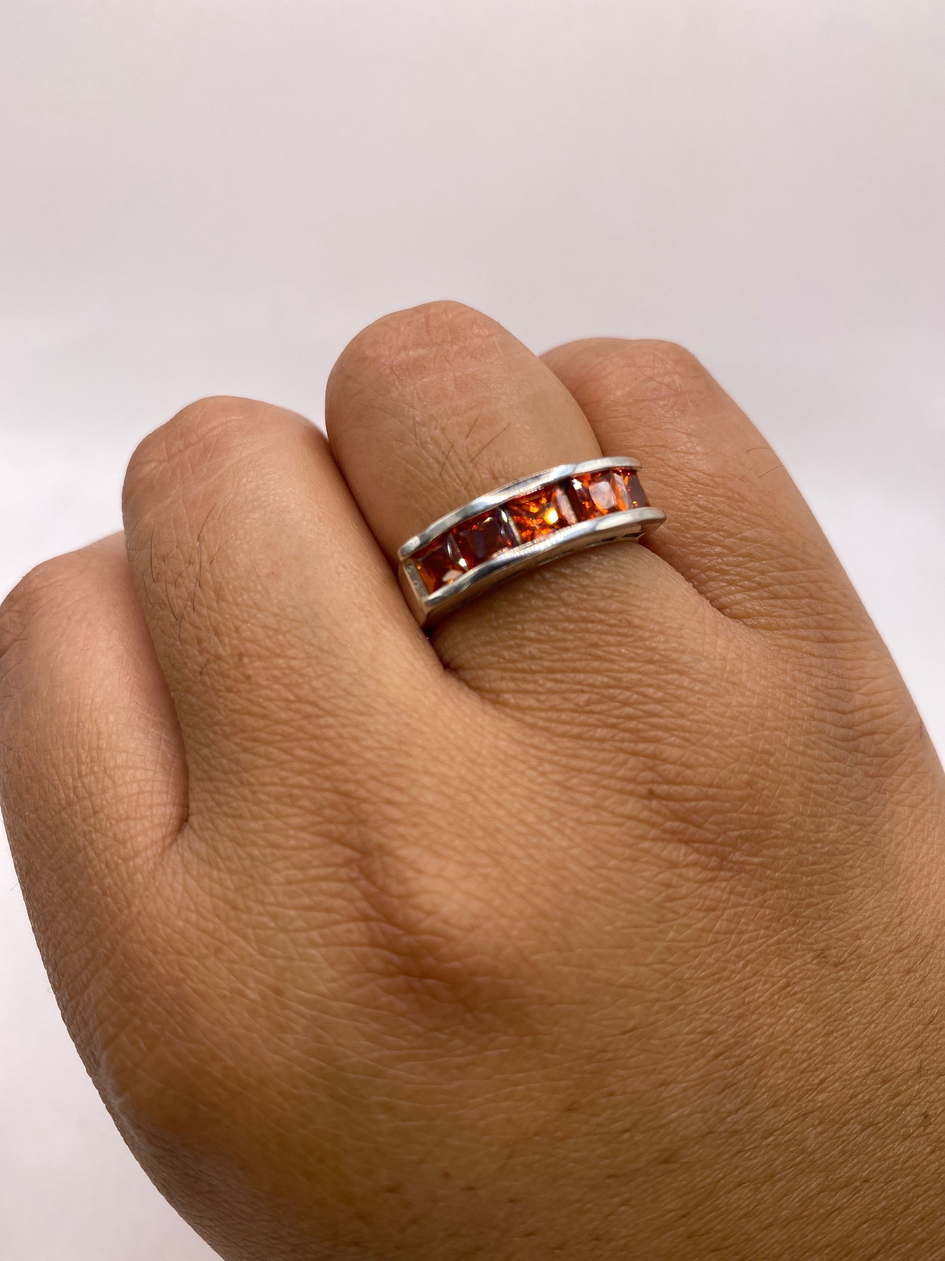 Anillo banda de plata con circonias naranja puesto en la mano de una mujer, talla 7