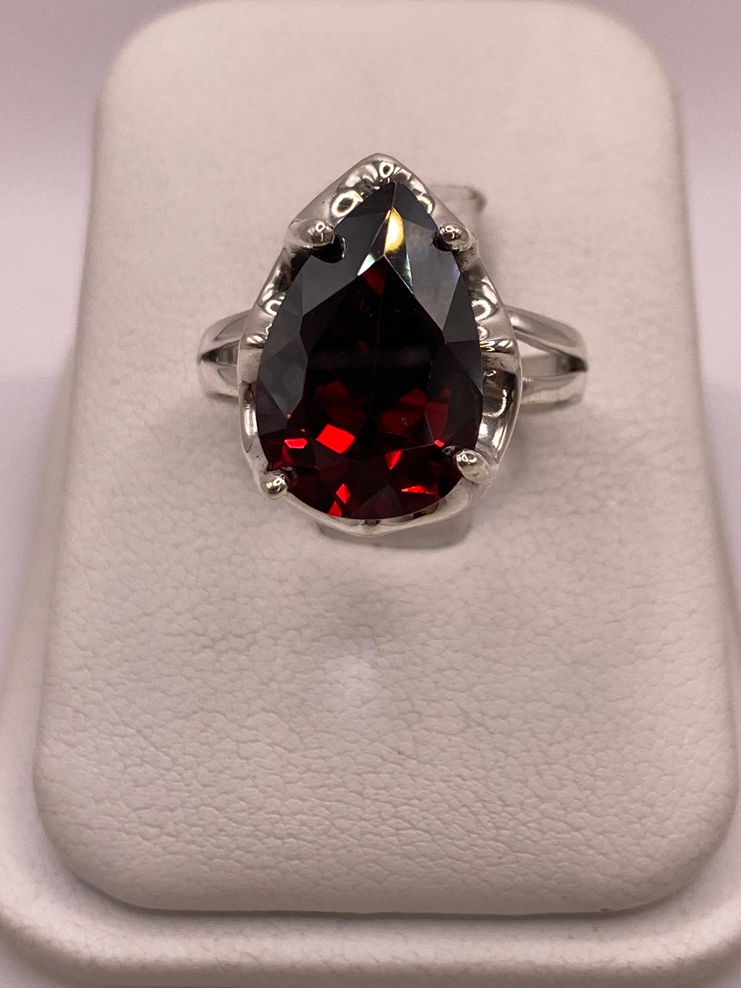 Anillo solitario de plata .925 con circonia roja corte pera en engaste de garra, vista frontal sobre display blanco