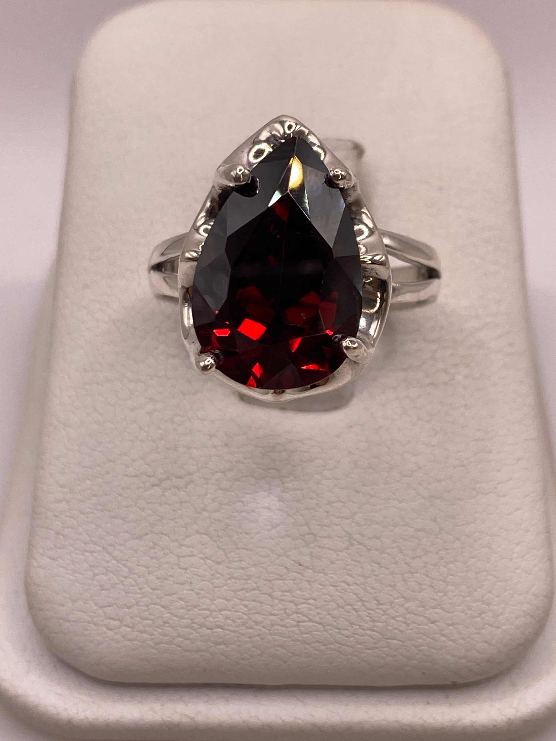 Anillo solitario de plata .925 con circonia roja corte pera en engaste de garra, vista frontal sobre display blanco