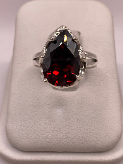 Anillo solitario de plata .925 con circonia roja corte pera en engaste de garra, vista frontal sobre display blanco
