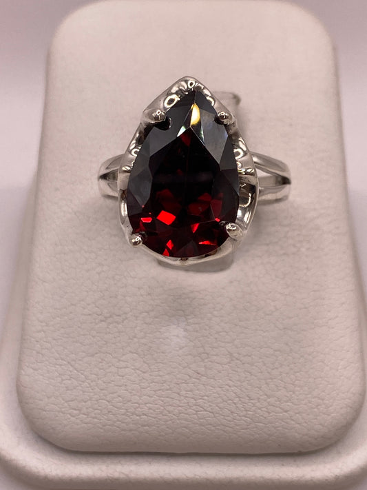 Anillo solitario de plata .925 con circonia roja corte pera en engaste de garra, vista frontal sobre display blanco