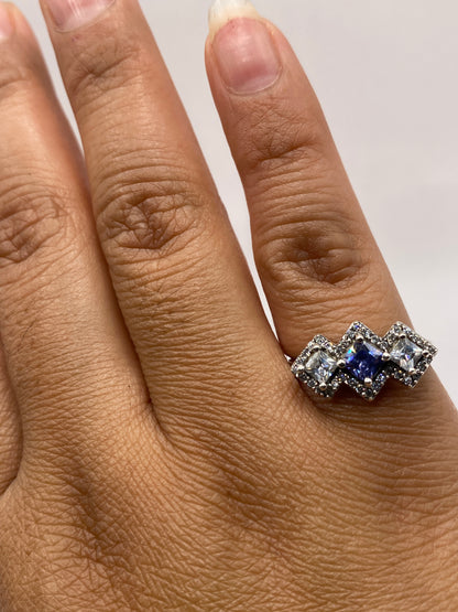 Anillo de plata tres circonias princess azul y blanco puesto en la mano de una mujer