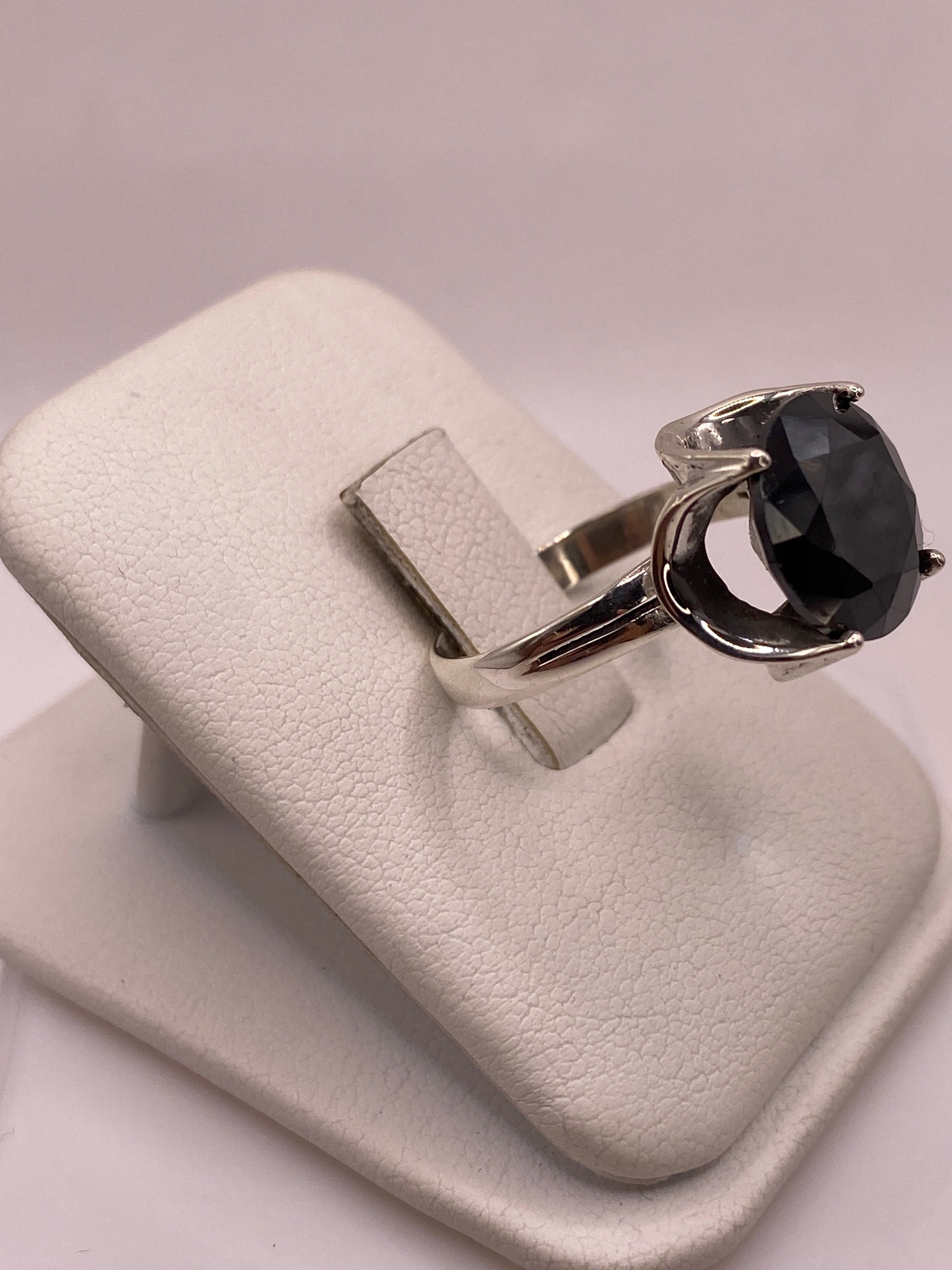 Anillo solitario de plata con circonia negra oval en soporte de joyería, vista lateral que muestra el engaste en garra