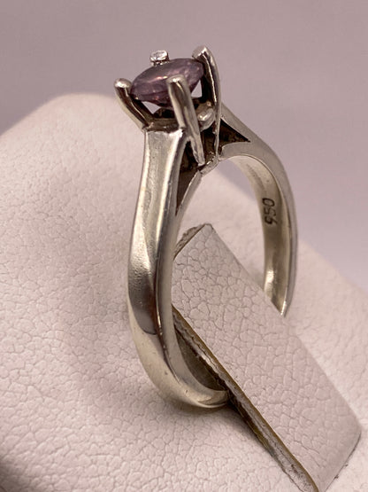 Detalle del engaste en plata del anillo con circonia morada brillando contra fondo gris