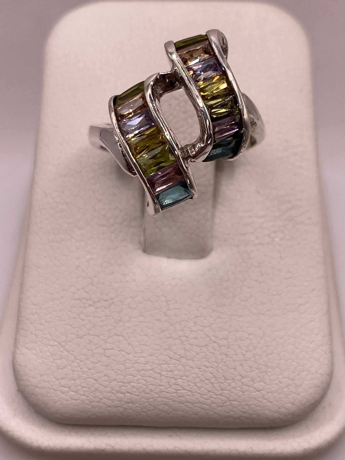 Anillo de plata solitario con circonias verdes y púrpuras en mano de mujer sobre fondo blanco