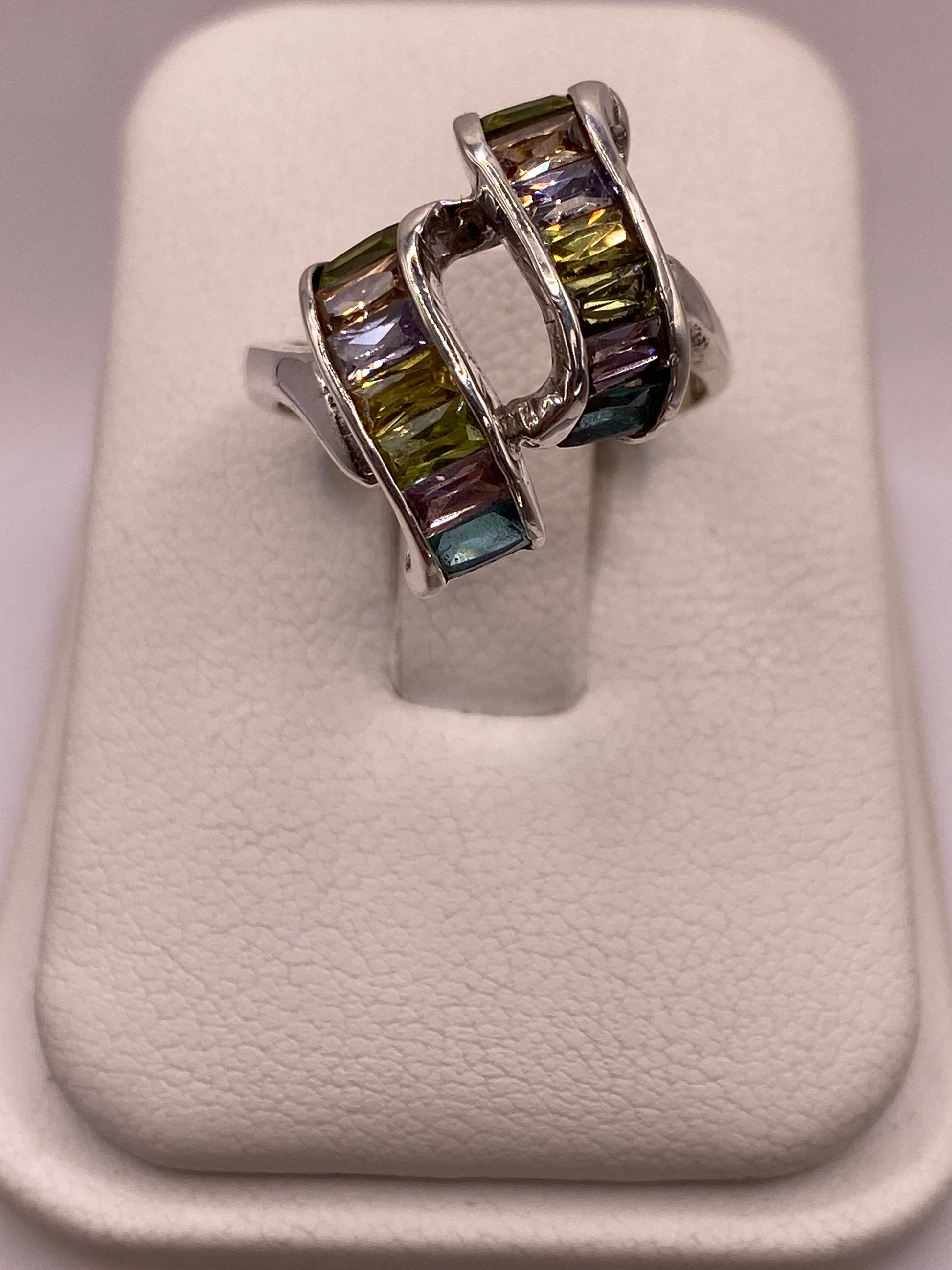 Anillo de plata solitario con circonias verdes y púrpuras en mano de mujer sobre fondo blanco