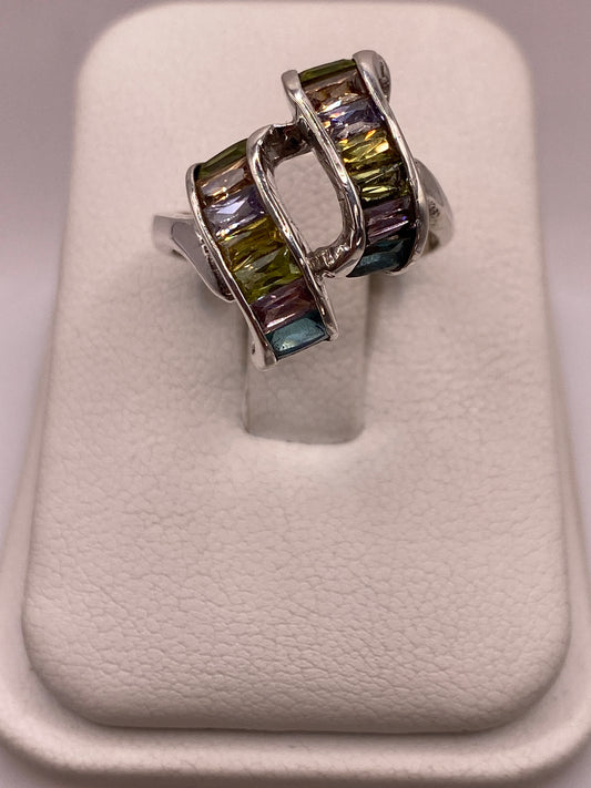 Anillo de plata solitario con circonias verdes y púrpuras en mano de mujer sobre fondo blanco