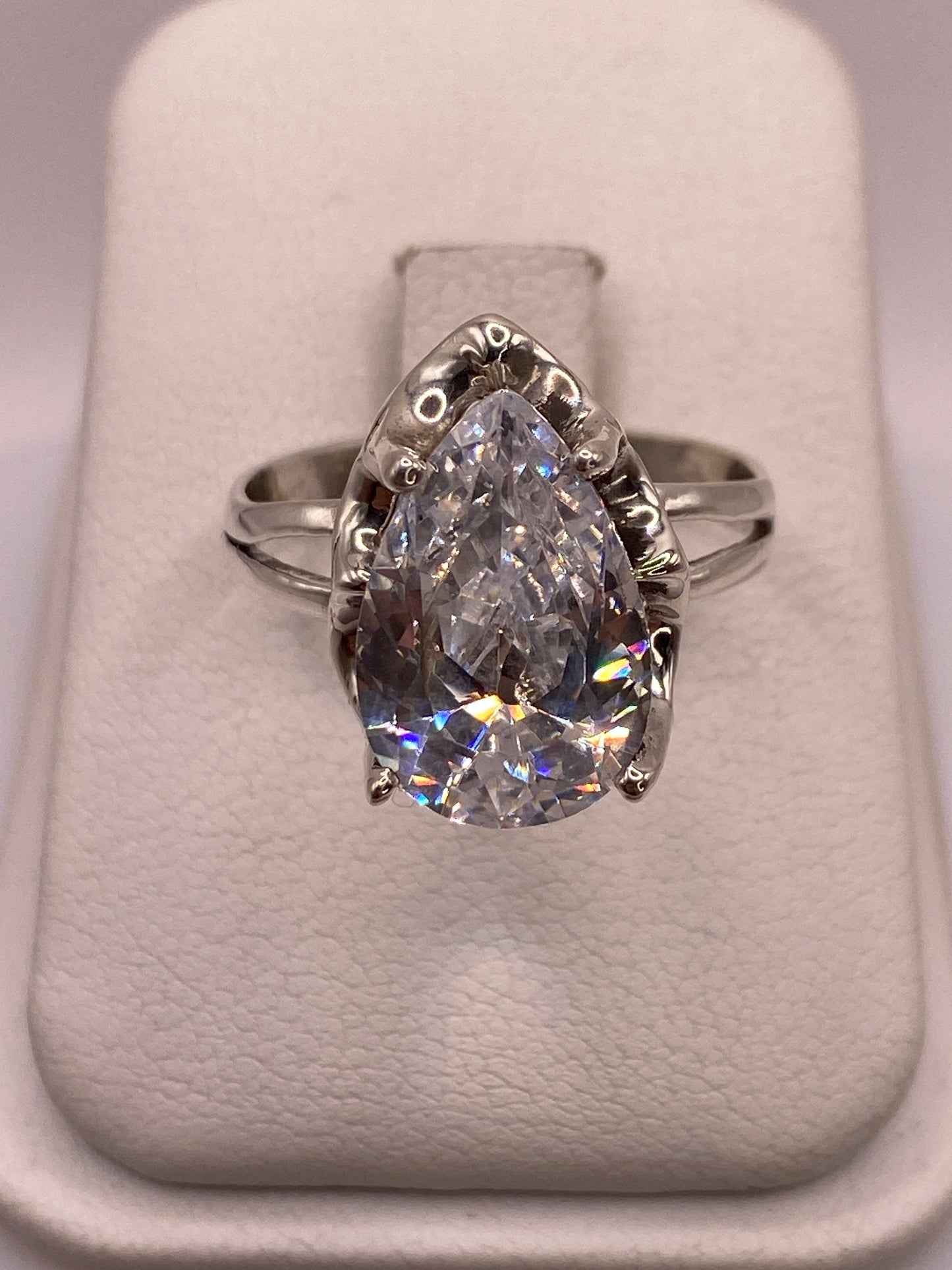 Anillo de plata solitario con circonia blanca corte gota, visto de frente sobre almohada blanca
