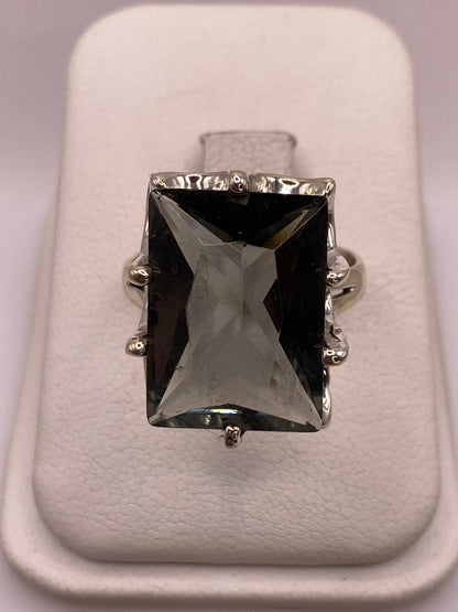 Anillo solitario de plata con circonia gris ahumado en forma rectangular facetada, posado en joyero blanco