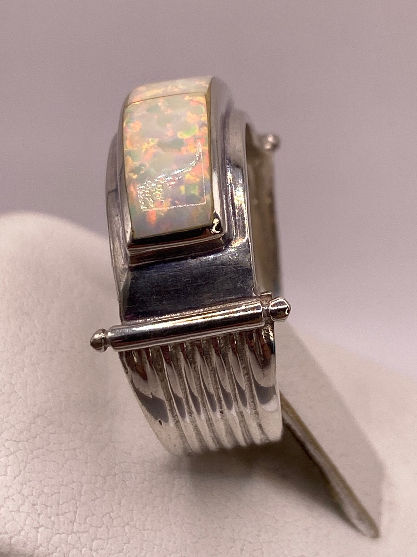 Anillo solitario con ópalo de fuego puesto en dedo, luz natural revelando juego de colores