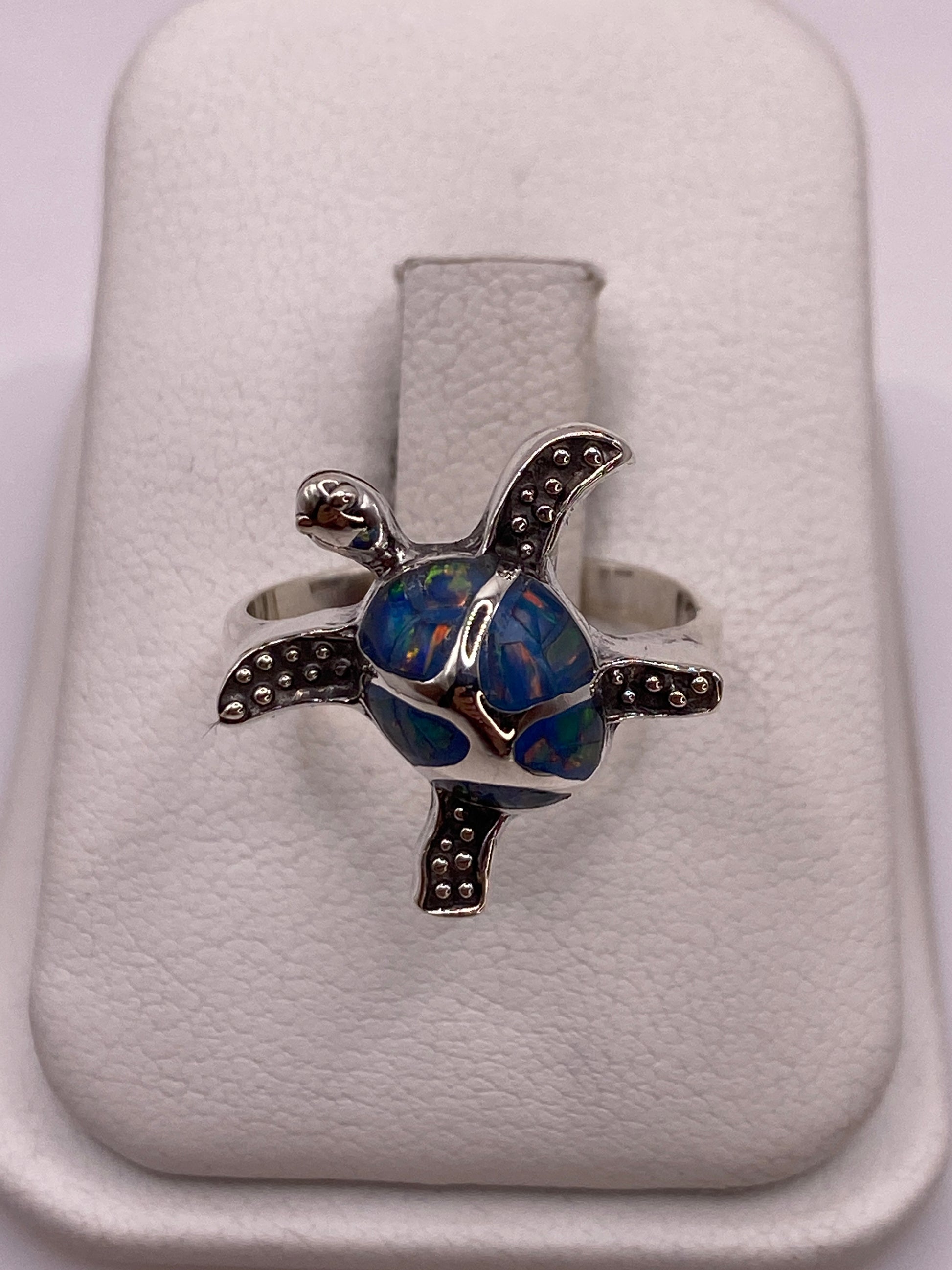 Anillo de plata con ópalo azul en forma de tortuga escultural, vista frontal sobre fondo blanco