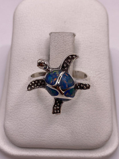 Anillo de plata con ópalo azul en forma de tortuga escultural, vista frontal sobre fondo blanco