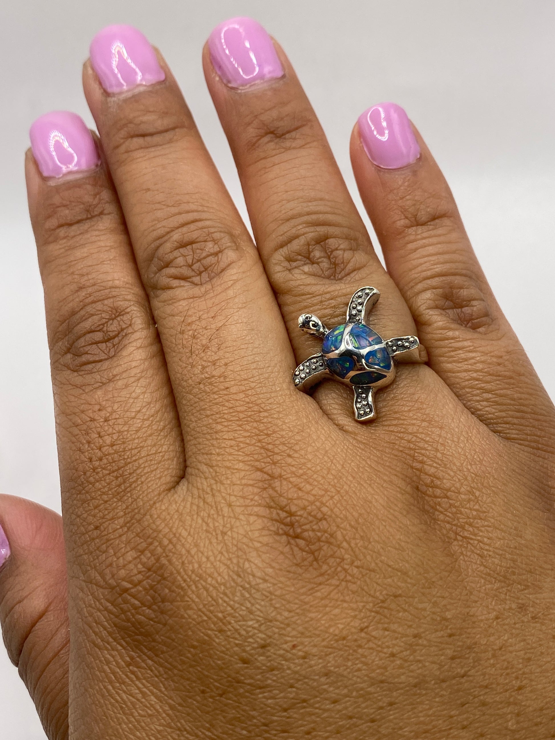 Anillo escultural de tortuga con ópalo azul en mano de mujer, mostrando movimiento de la gema