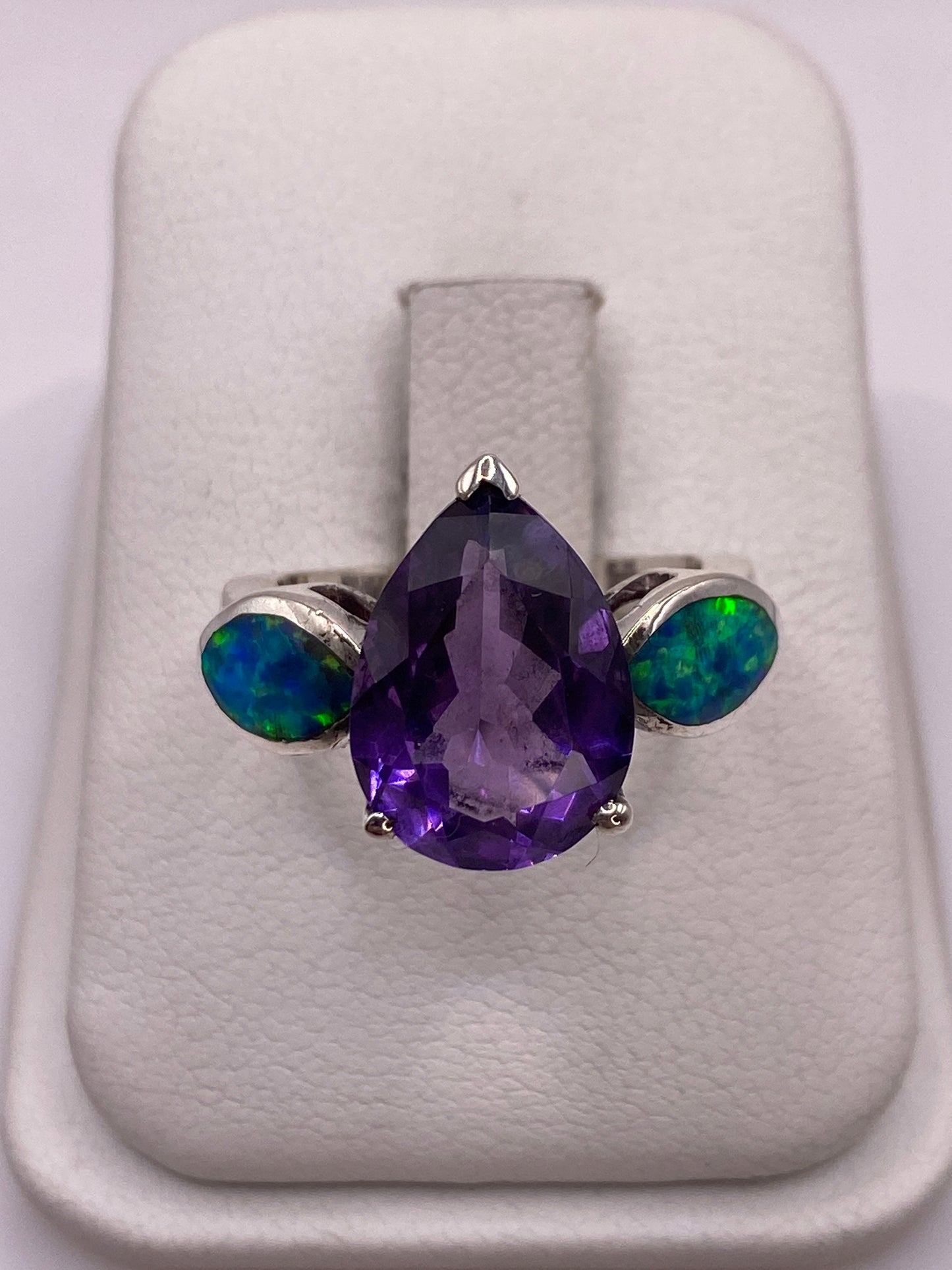 Anillo de plata con ópalo de fuego púrpura en bandeja blanca, mostrando el juego de colores