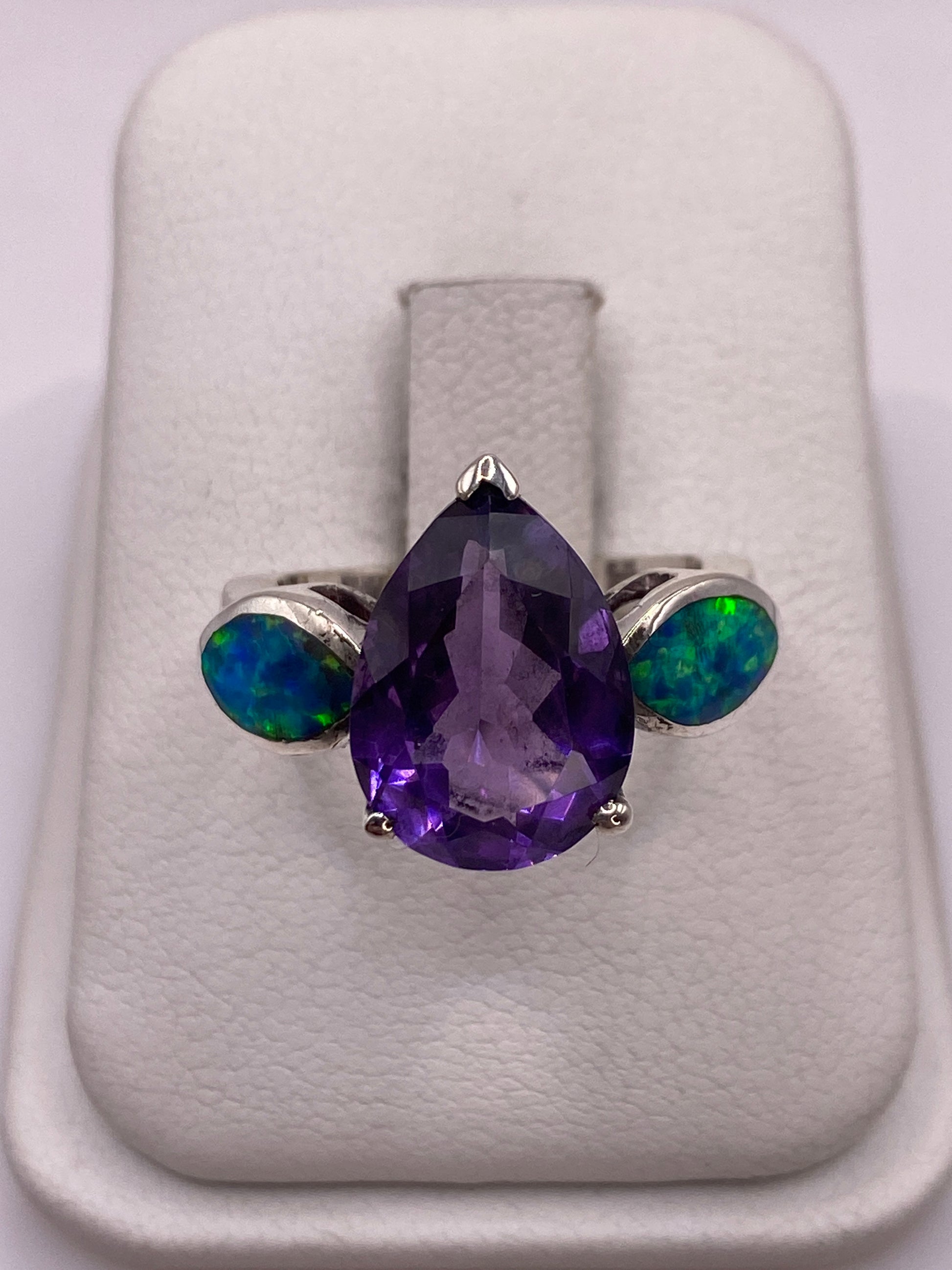 Anillo de plata con ópalo de fuego púrpura en bandeja blanca, mostrando el juego de colores