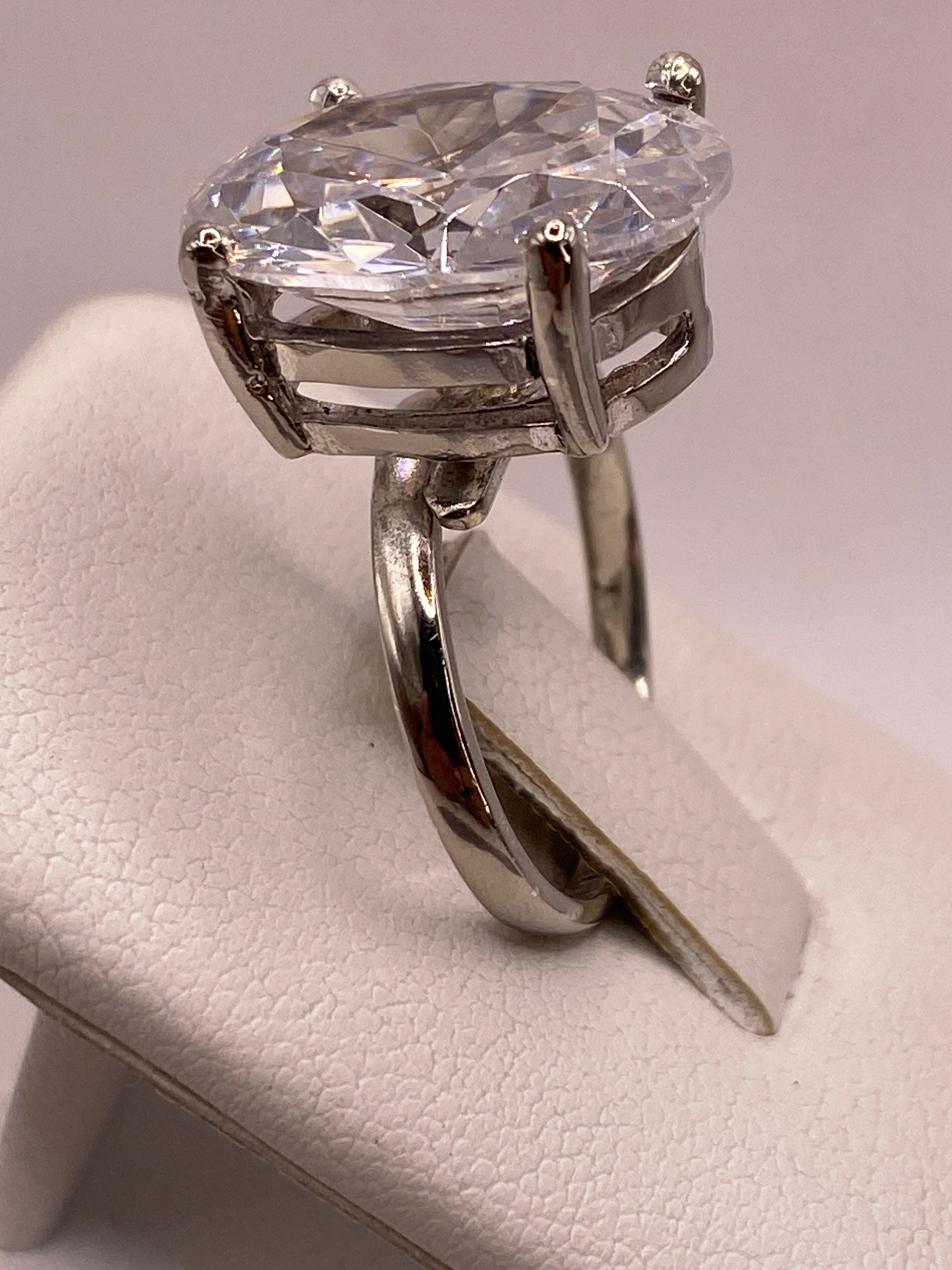 Anillo solitario en el dedo de una mujer con esmalte rosa, luz reflejada en la piedra