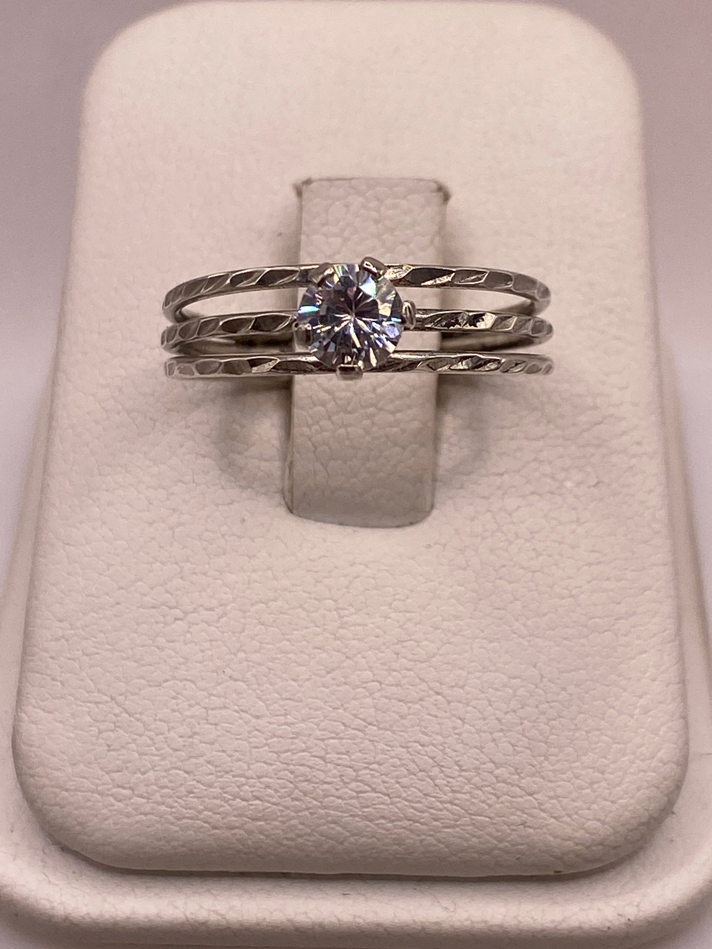 Anillo de plata solitario con circonia blanca en mano de mujer con uñas rosa