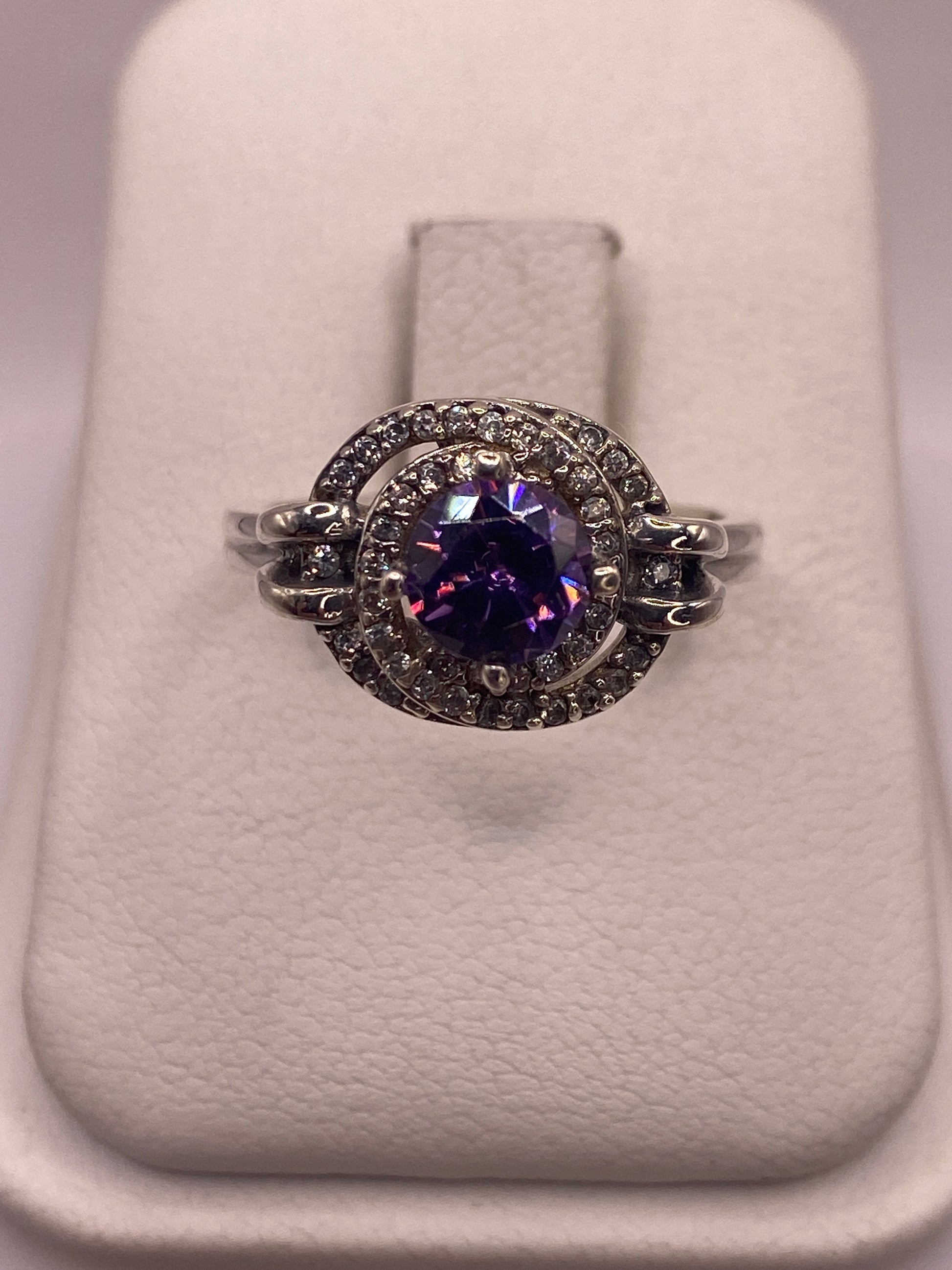 Anillo de plata solitario con circonia morada en la mano de una mujer sobre fondo blanco