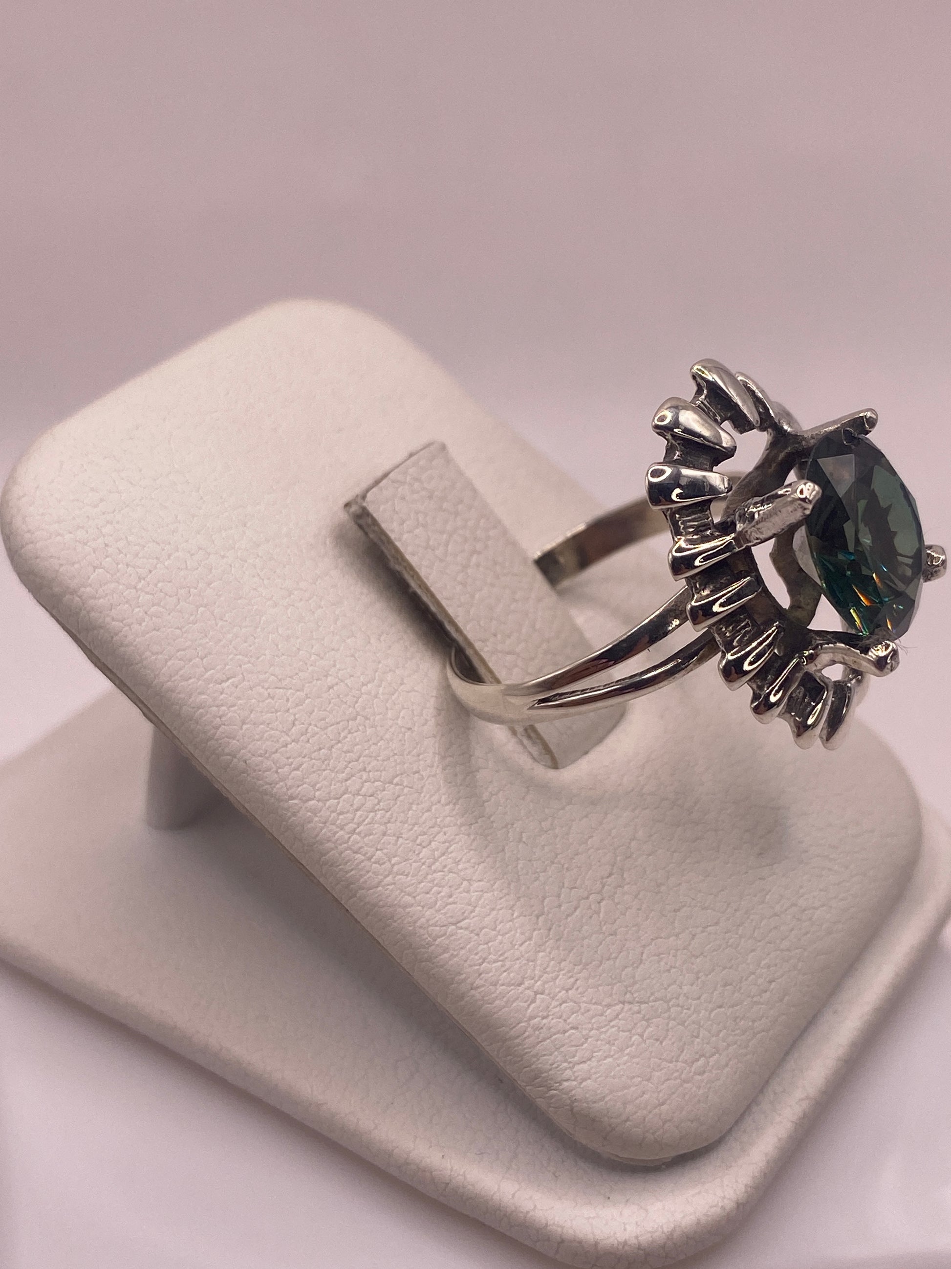 Anillo solitario verde en la mano, mostrando el halo escalonado en plata