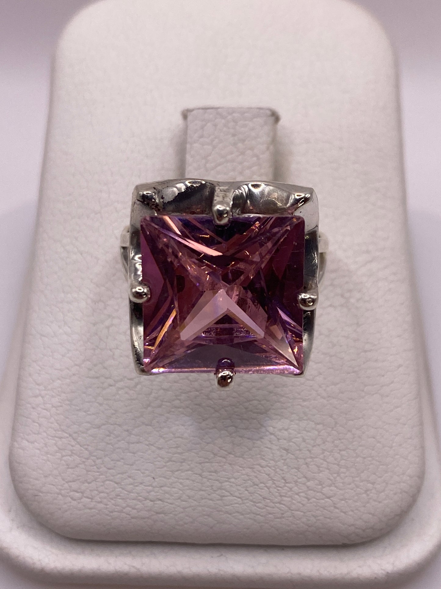 Anillo de plata solitario con circonia rosa facetada, vista frontal sobre cojín blanco