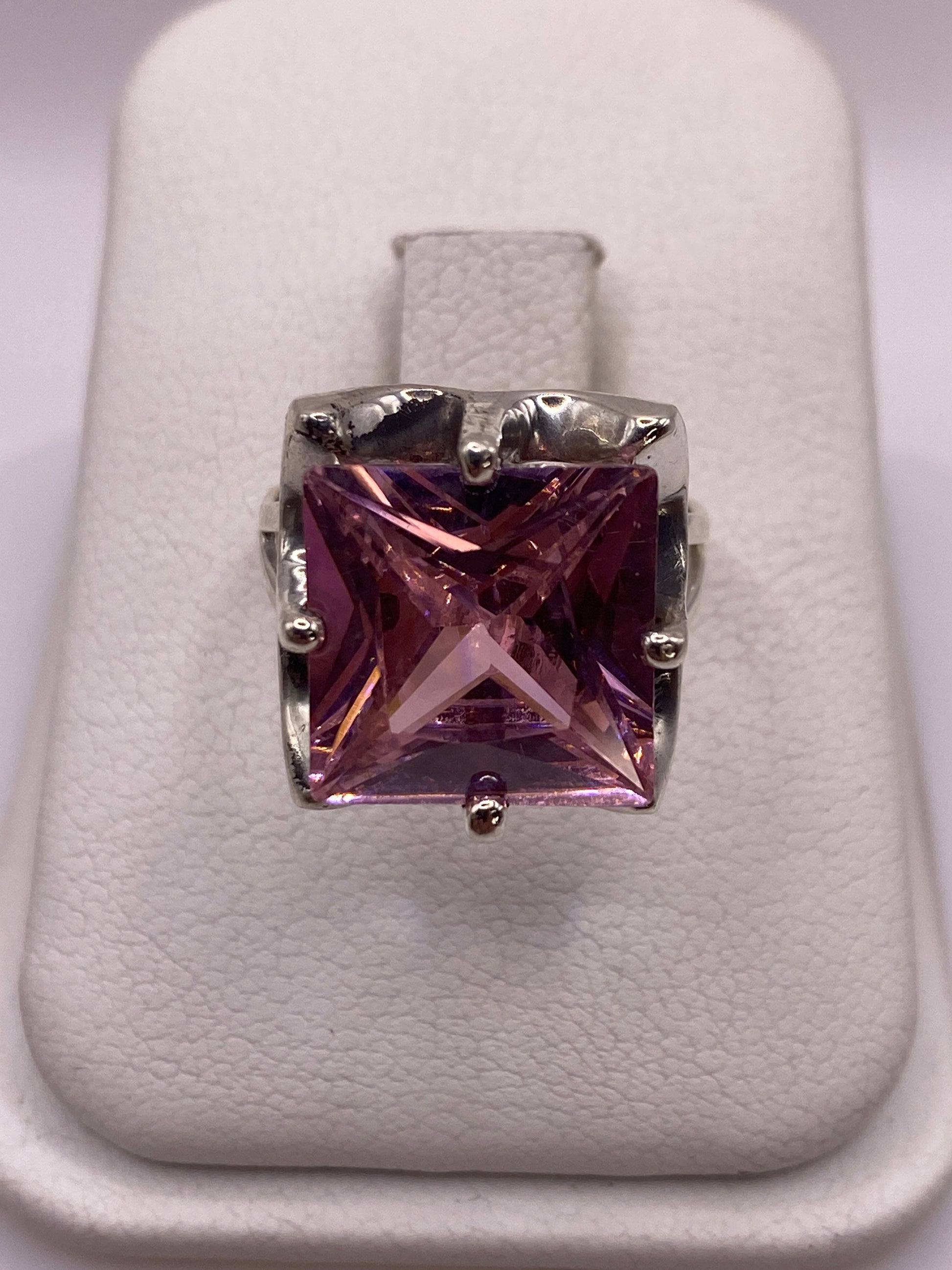 Anillo de plata solitario con circonia rosa facetada, vista frontal sobre cojín blanco