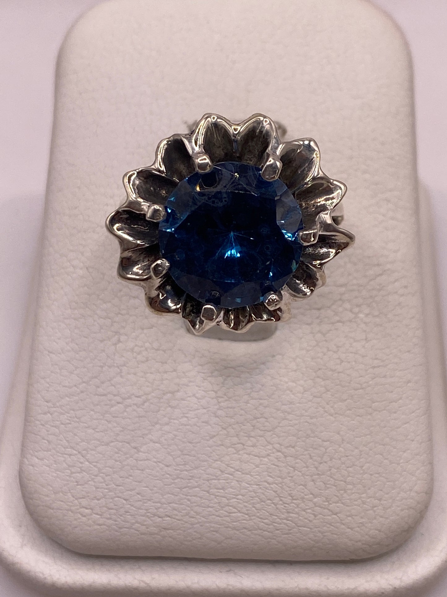Anillo solitario de plata con circonia azul facetada sobre fondo blanco