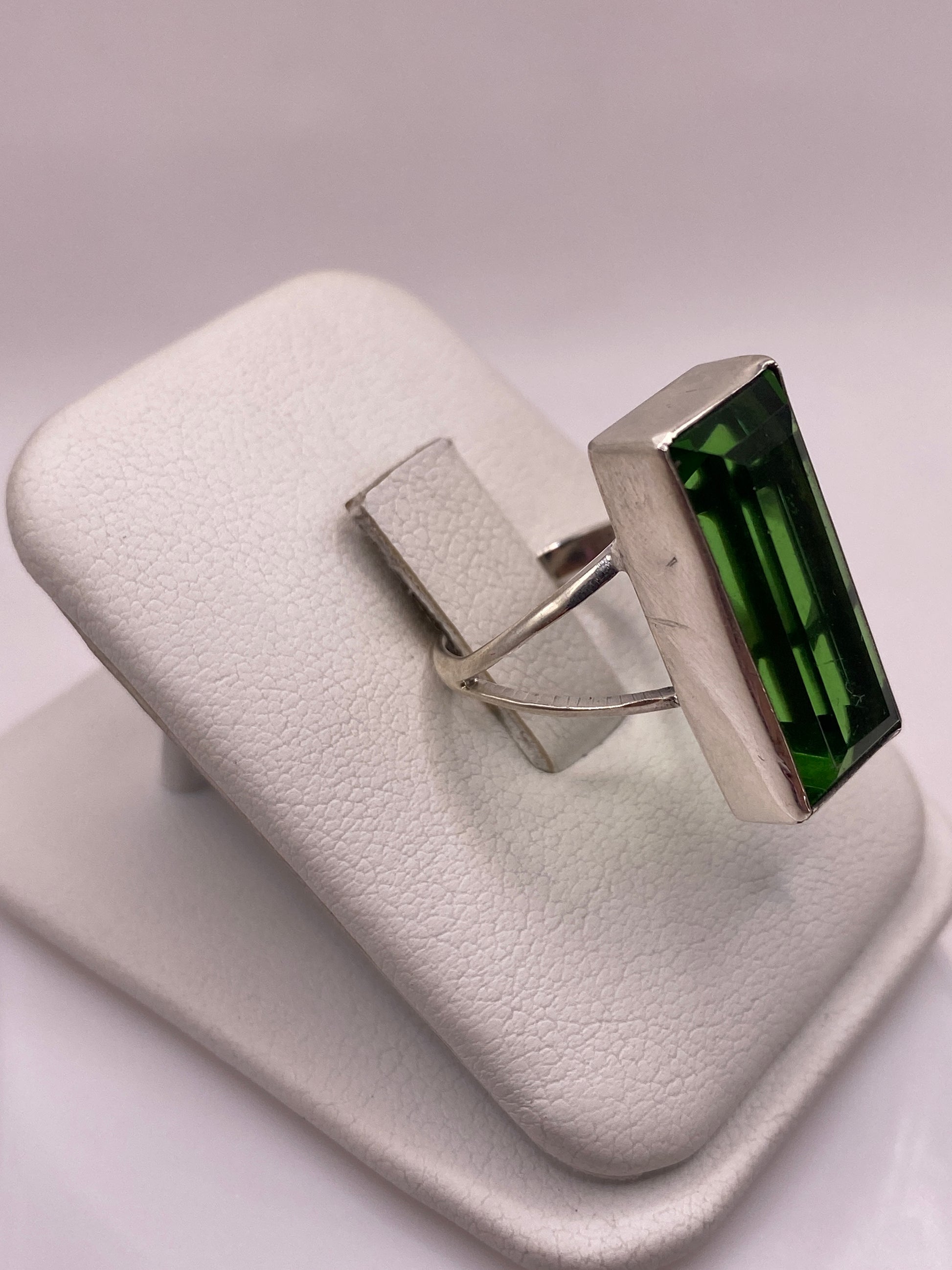 Anillo de plata .925 con piedra verde rectangular en la mano, mostrando el brillo de la circonia