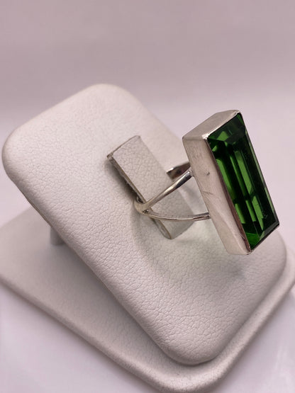 Anillo de plata .925 con piedra verde rectangular en la mano, mostrando el brillo de la circonia