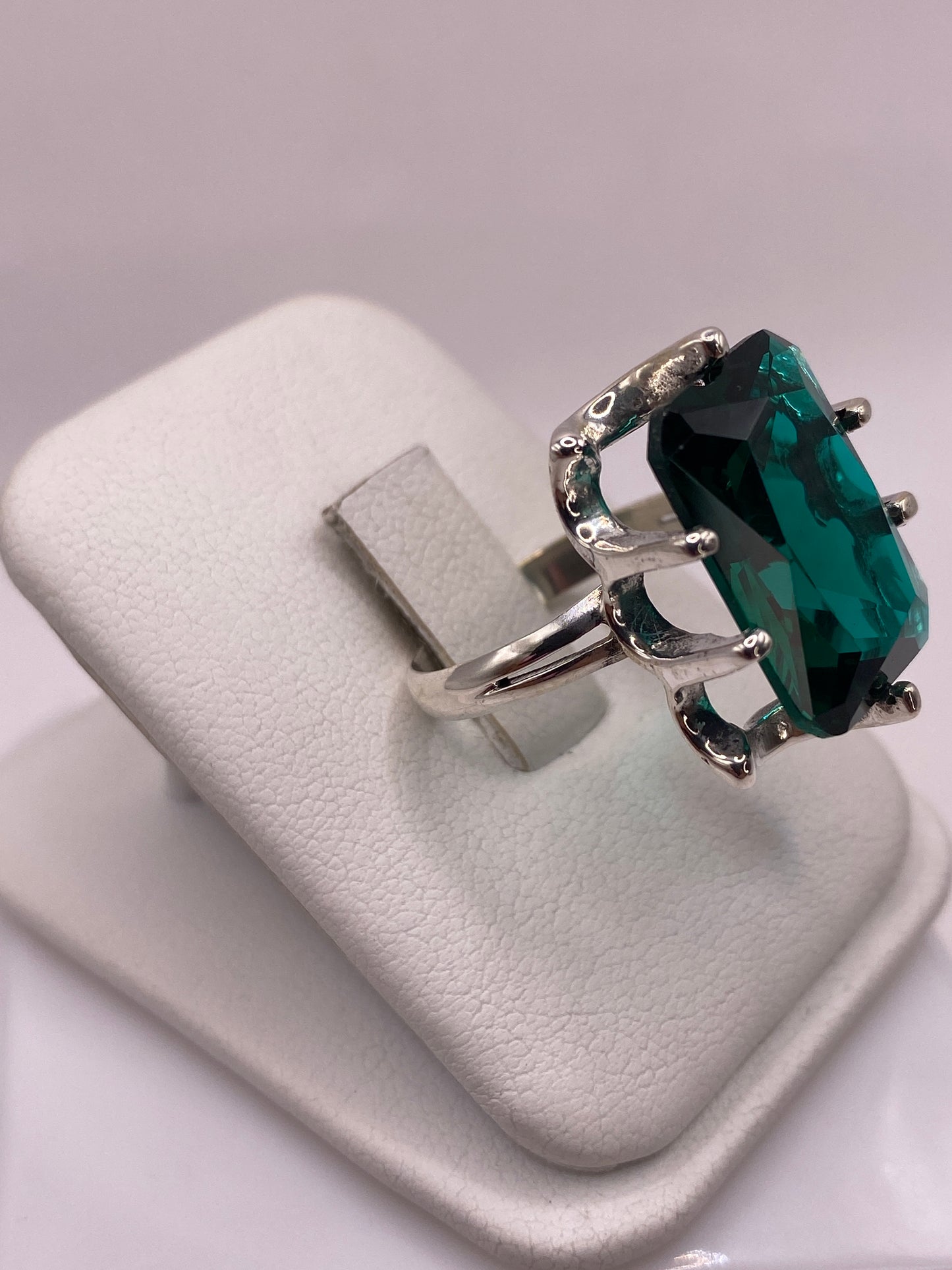 Vista frontal del anillo circonia verde con engaste ornamental de plata en la mano