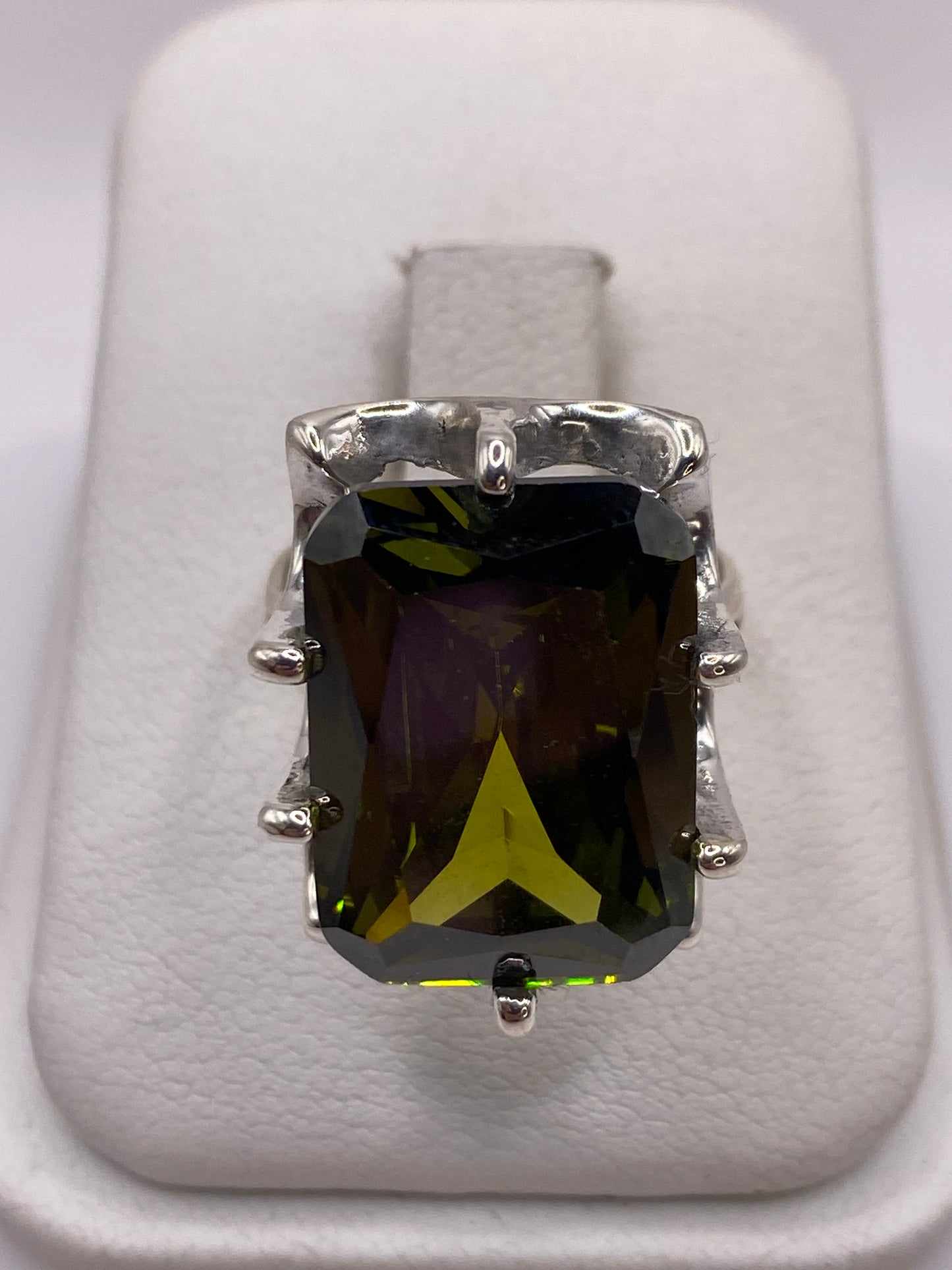 Anillo de plata solitario con circonia verde olivo facetada sobre almohada blanca