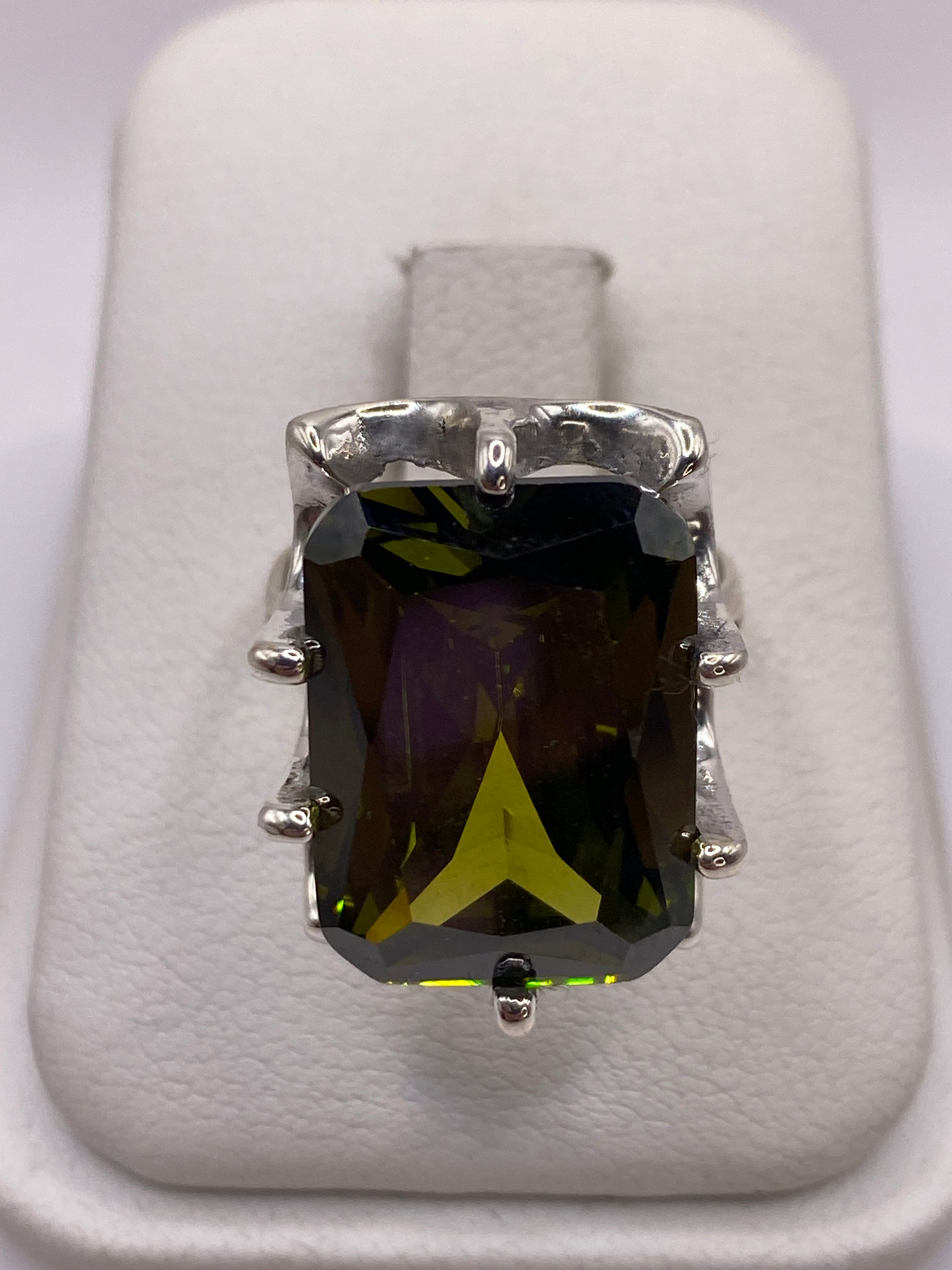 Anillo de plata solitario con circonia verde olivo facetada sobre almohada blanca