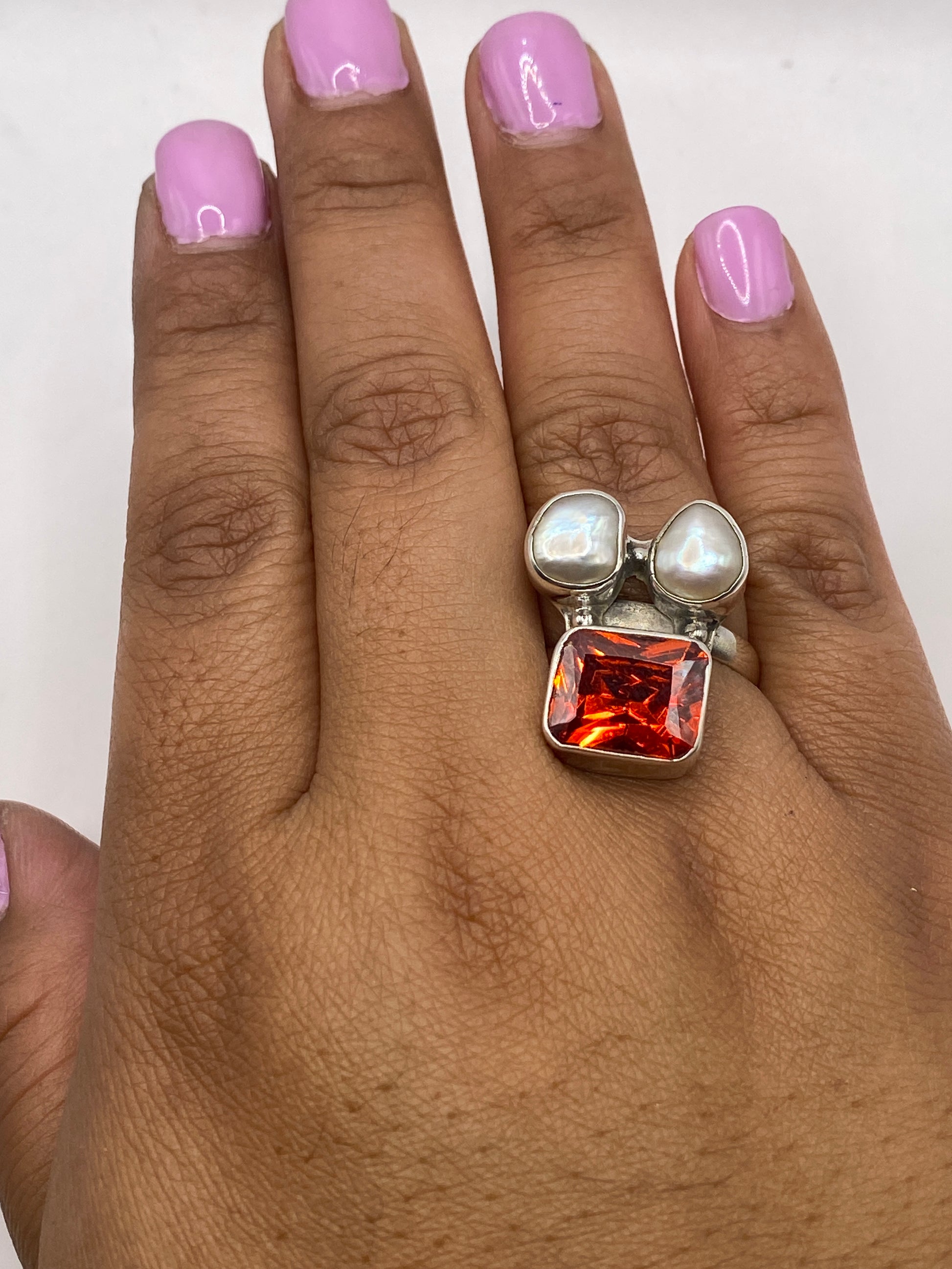Anillo en la mano de mujer luciendo el contraste entre la perla y la gema naranja