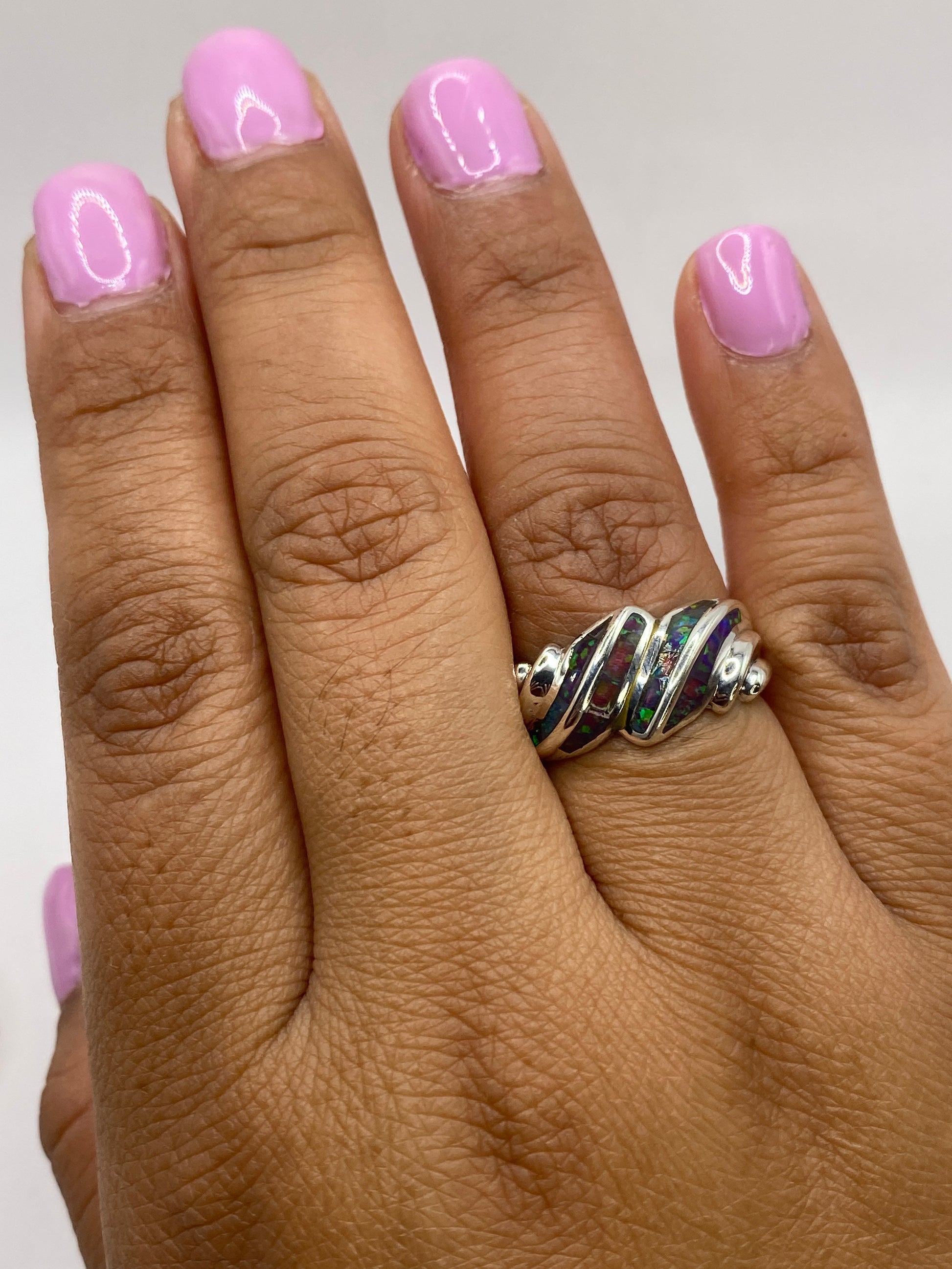 Anillo en mano femenina con uñas rosa, destacando el cambio de colores del ópalo bajo luz natural