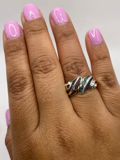 Anillo en mano femenina con uñas rosa, destacando el cambio de colores del ópalo bajo luz natural