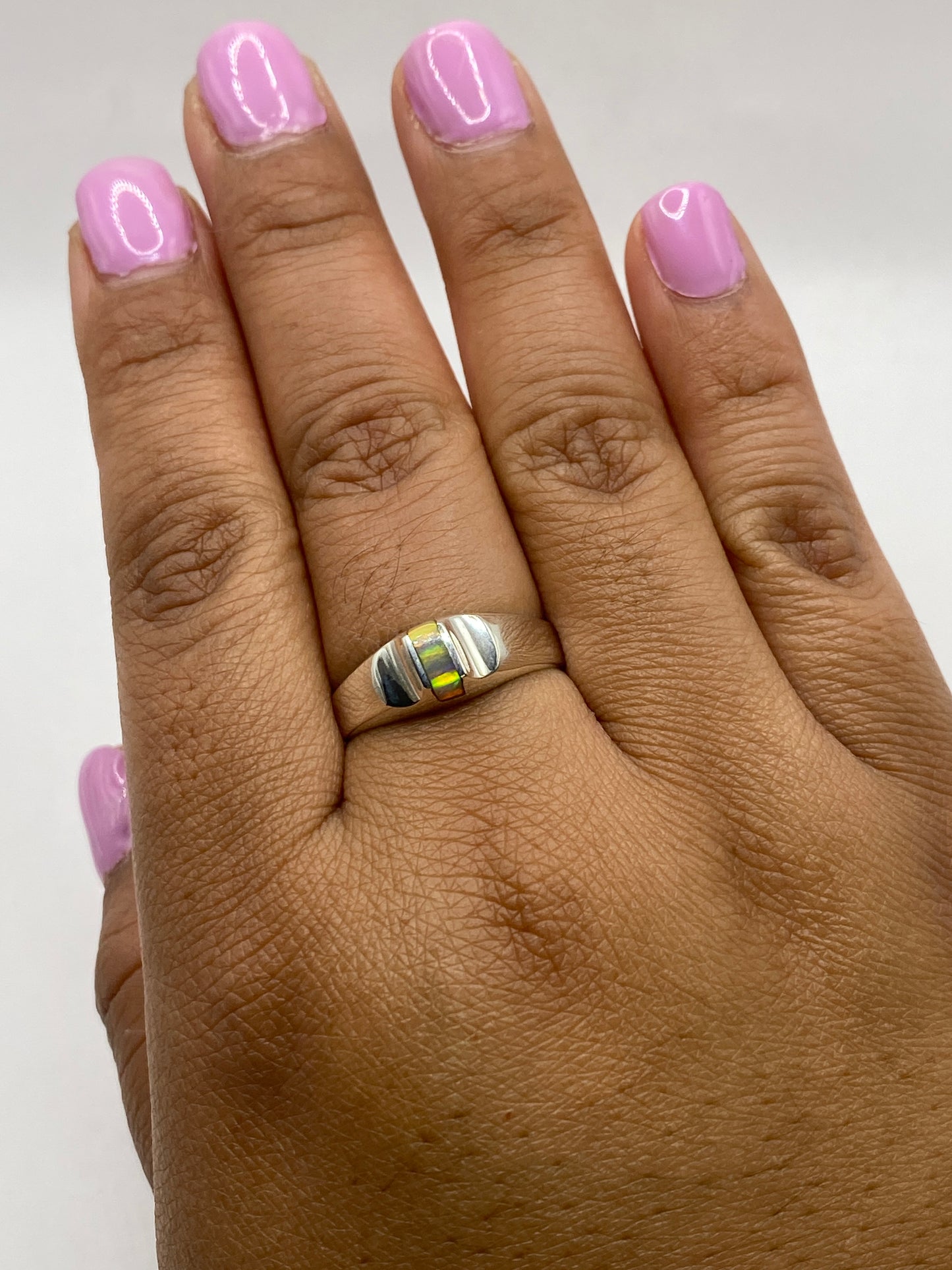 Anillo ópalo de fuego en mano con uñas rosas, mostrando el brillo reflejado de la piedra