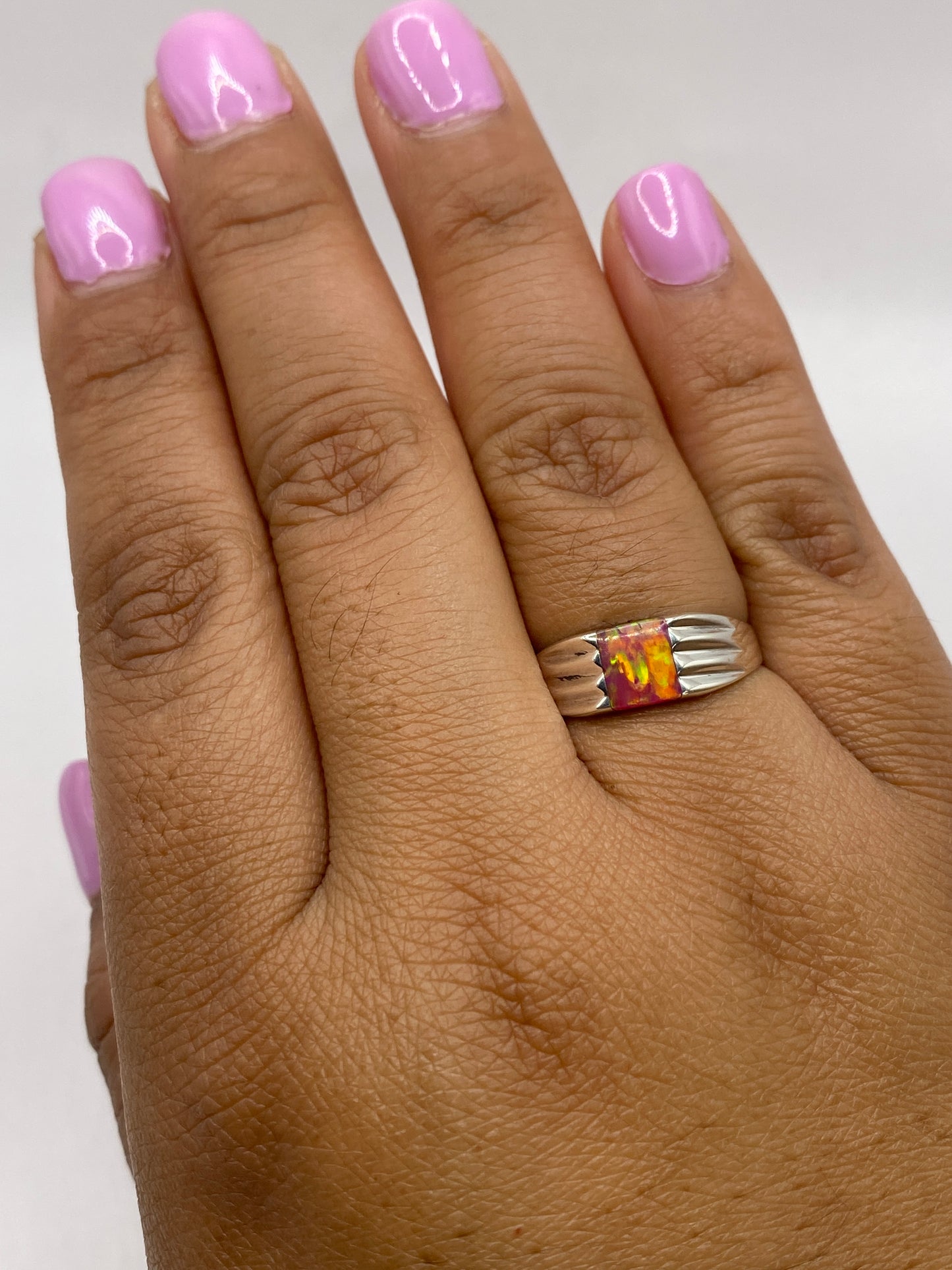 Anillo en la mano mostrando el juego de color del ópalo bajo luz natural