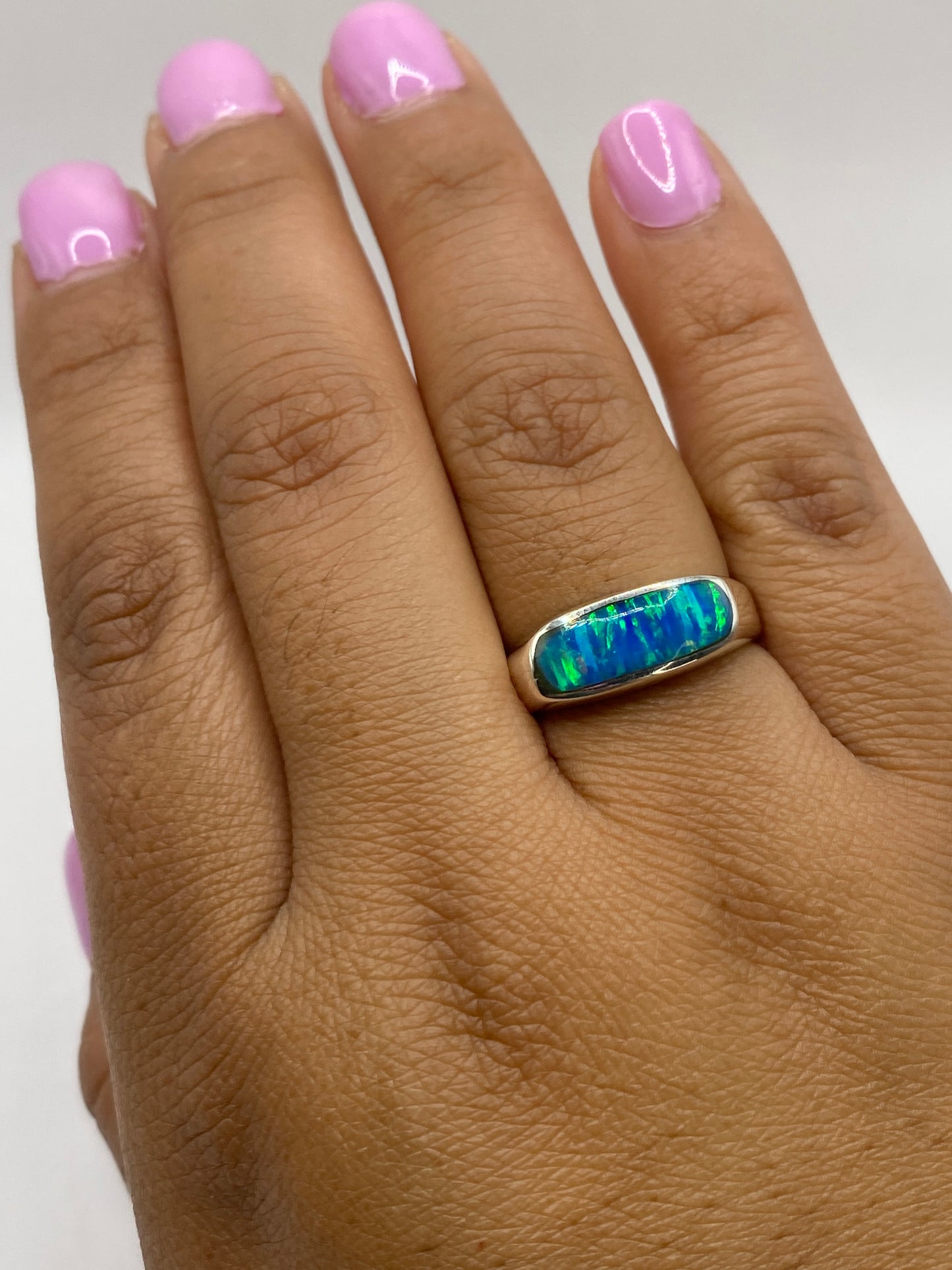 Anillo sobre dedo con nail art rosa, mostrando el fuego azul del ópalo