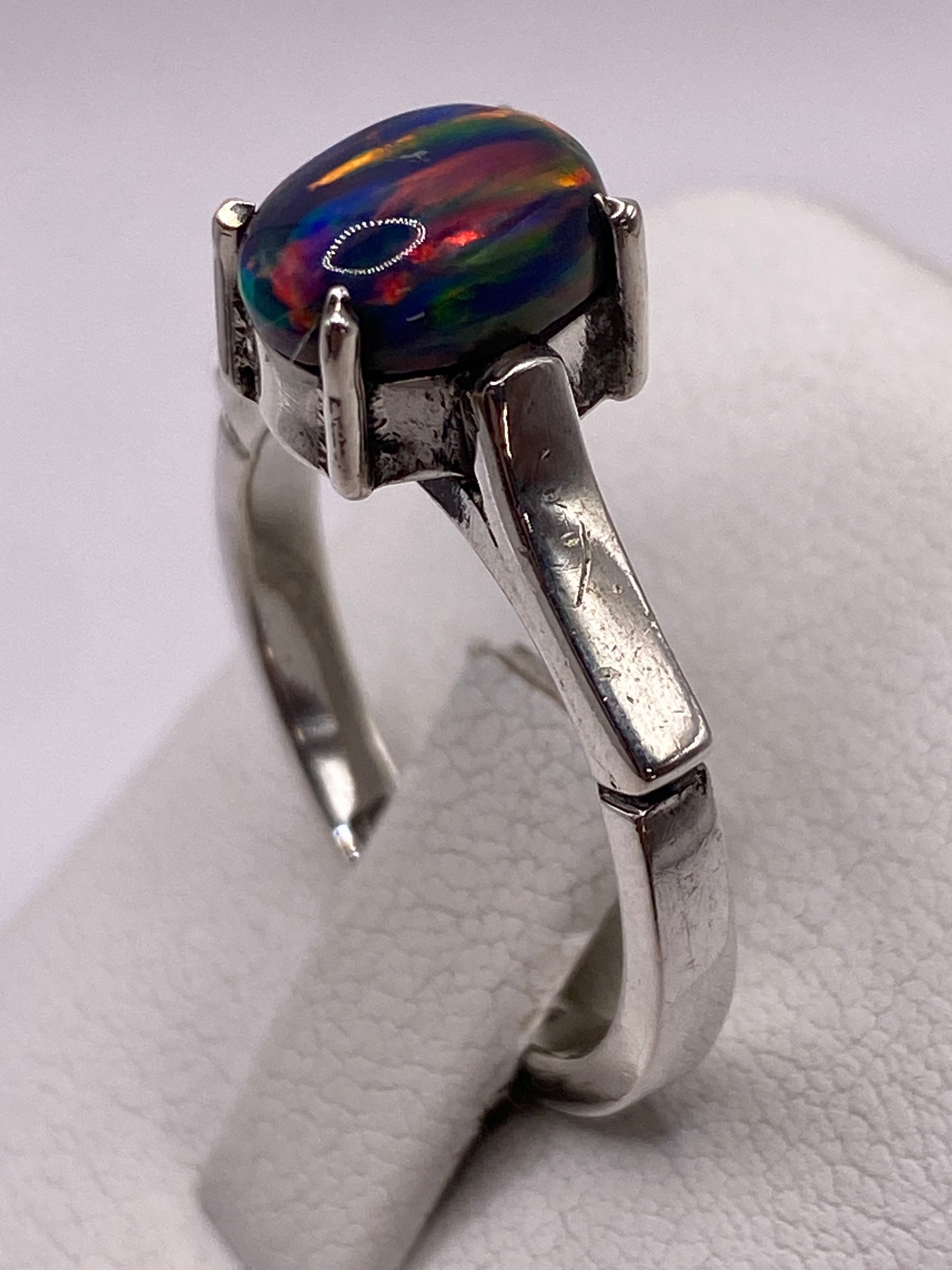 Anillo solitario en la mano de una mujer con uñas rosa, ópalo brillando con luz natural