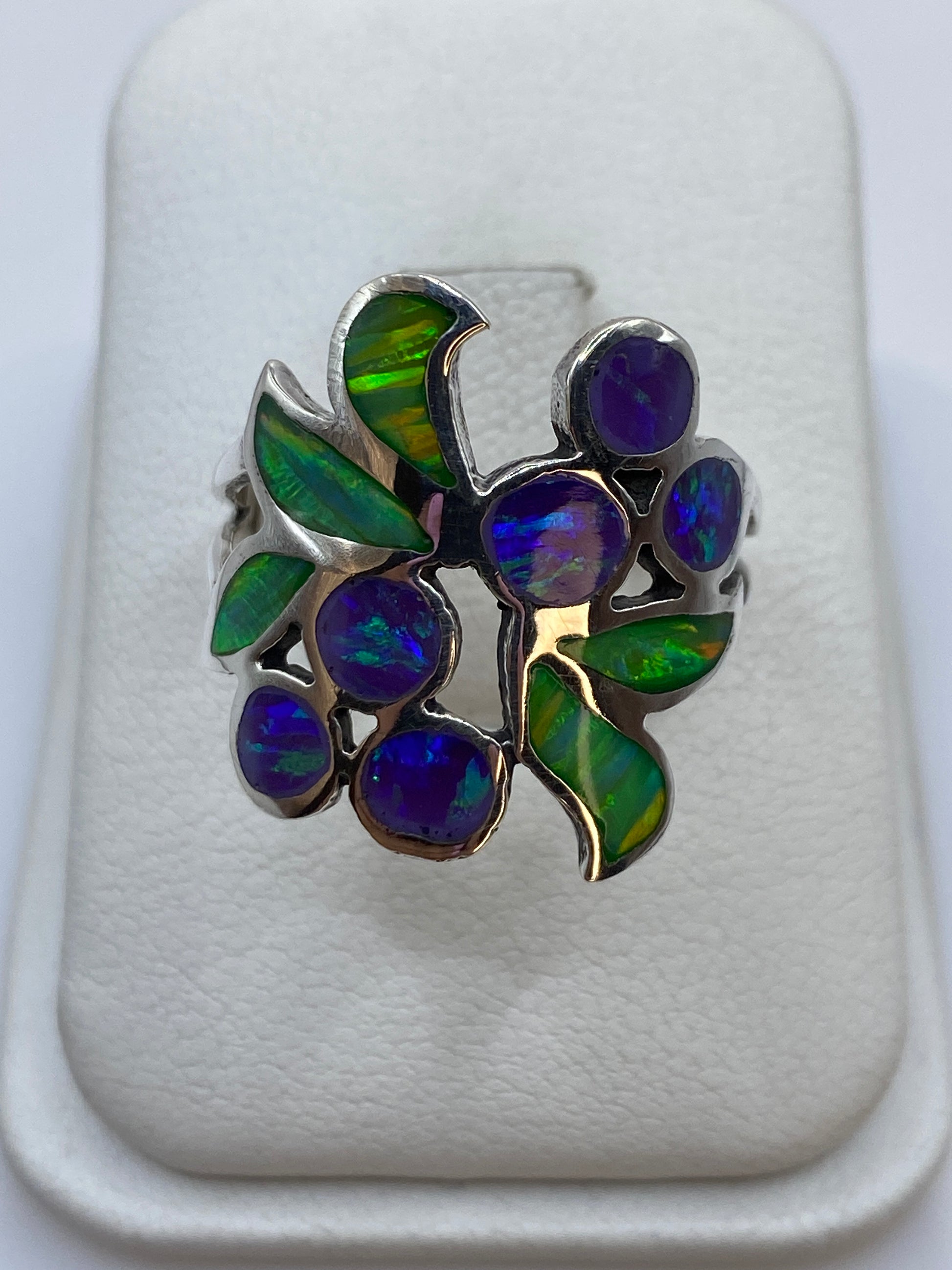 Anillo de plata con ópalo de fuego morado y verde en diseño floral sobre fondo blanco