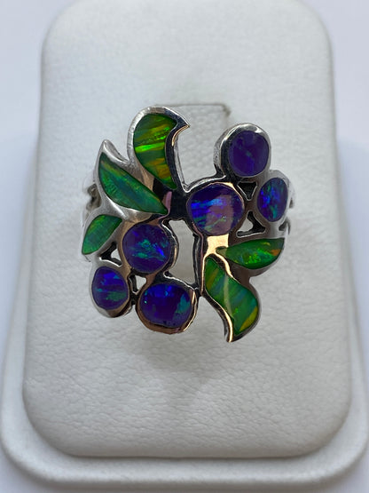 Anillo de plata con ópalo de fuego morado y verde en diseño floral sobre fondo blanco