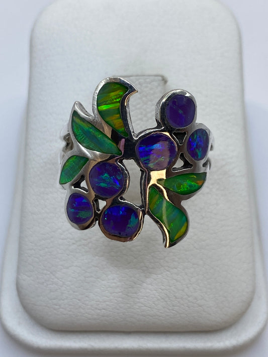 Anillo de plata con ópalo de fuego morado y verde en diseño floral sobre fondo blanco