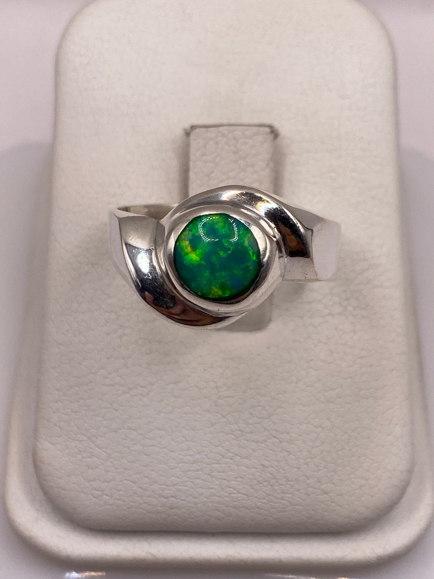 Anillo de plata .950 con ópalo de fuego verde en la mano, mostrando el juego de colores natural