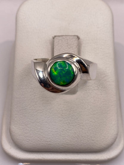 Anillo de plata .950 con ópalo de fuego verde en la mano, mostrando el juego de colores natural