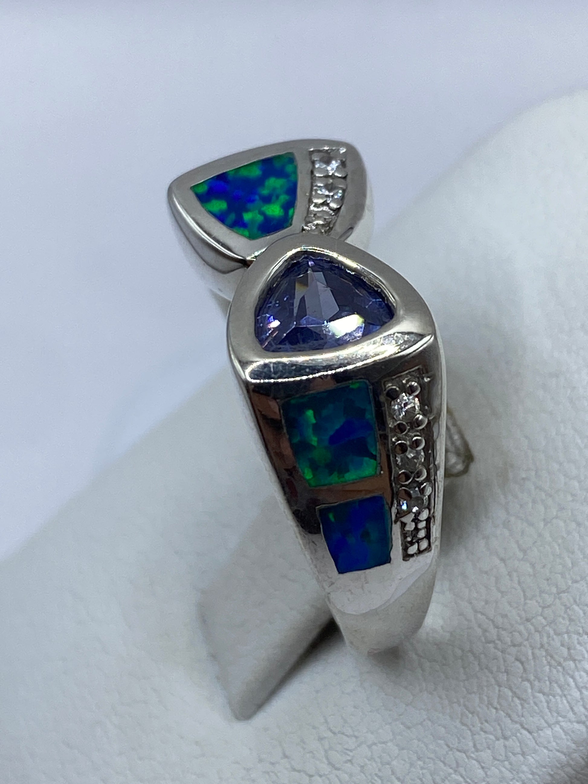 Anillo en la mano luciendo los reflejos azules y verdes del ópalo bajo la luz